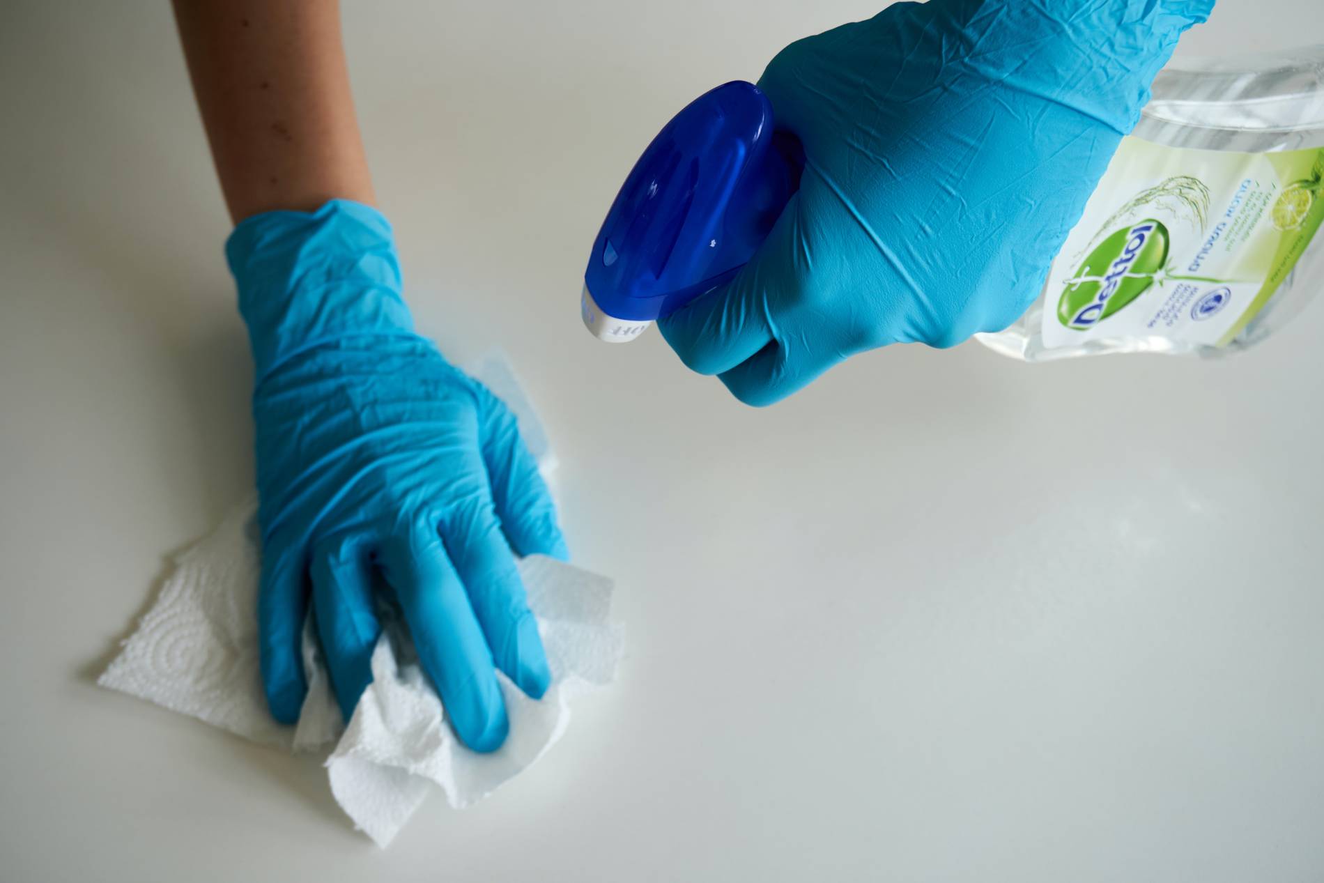 Person wearing gloves, holding a spray bottle and paper towel